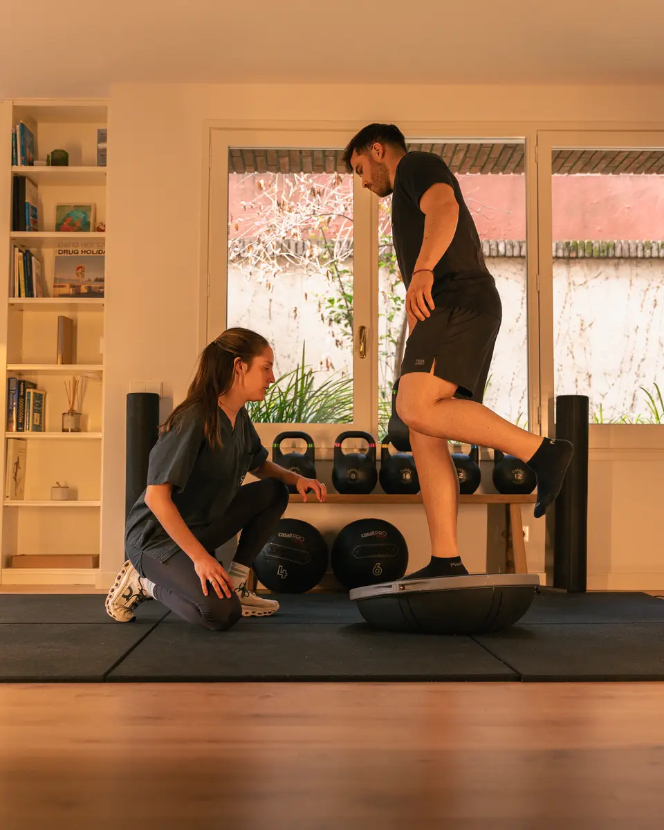 Fisioterapeuta controlando el equilibrio de un paciente sobre una pierna en un bosu